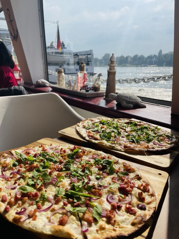 Flammkuchen Elsässer Art mit Speck und roten Zwiebeln auf dem Holzbrett am Fenster zum Rhein